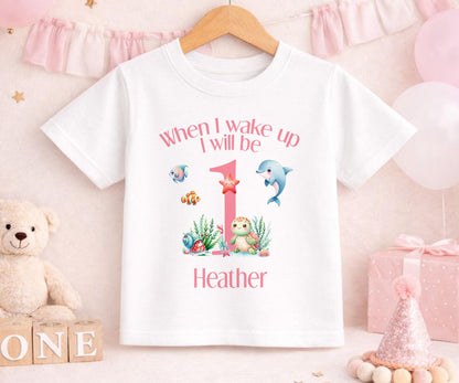 Personalised first birthday sleepsuit with custom name, laid flat to show the print.
