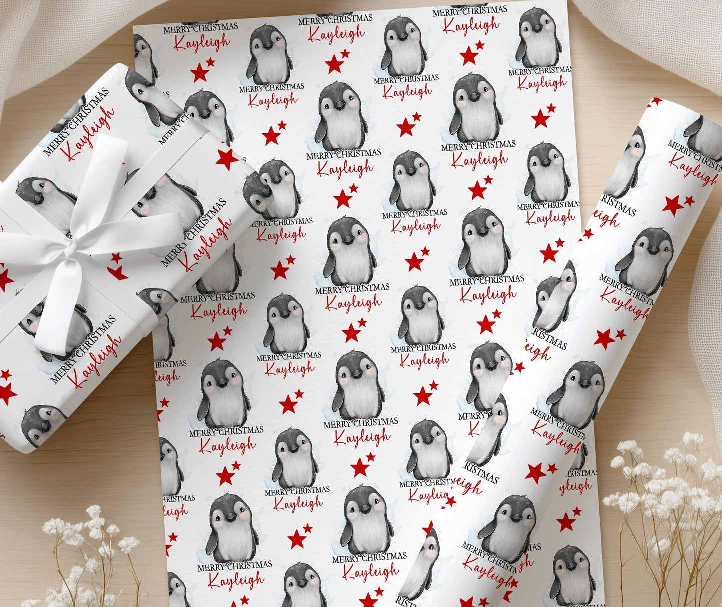 Personalised penguin Christmas wrapping paper printed with the name Kayleigh, shown on a wrapped gift finished with a white bow