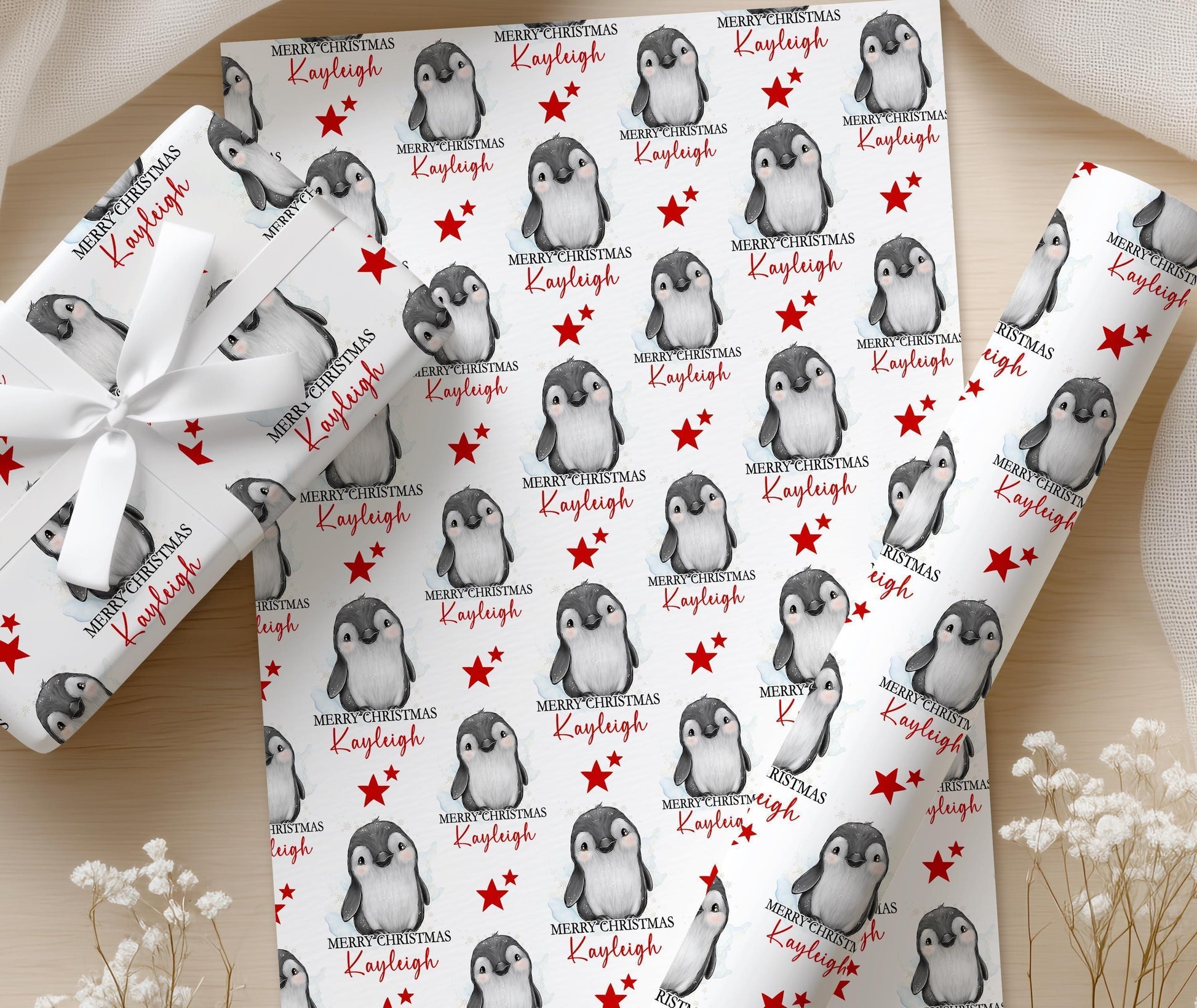 Personalised penguin Christmas wrapping paper printed with the name Kayleigh, shown on a wrapped gift finished with a white bow