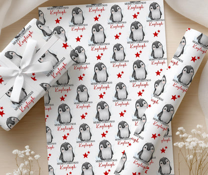 Personalised penguin Christmas wrapping paper printed with the name Kayleigh, shown on a wrapped gift finished with a white bow