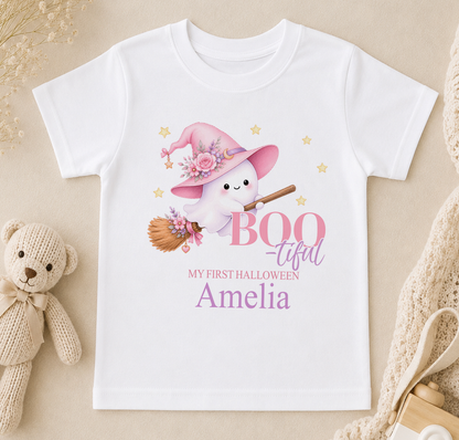 A white t-shirt with a cartoon ghost wearing a witch's hat and holding a broom, along with the text "BOO - TIFUL Amelia" printed on it.