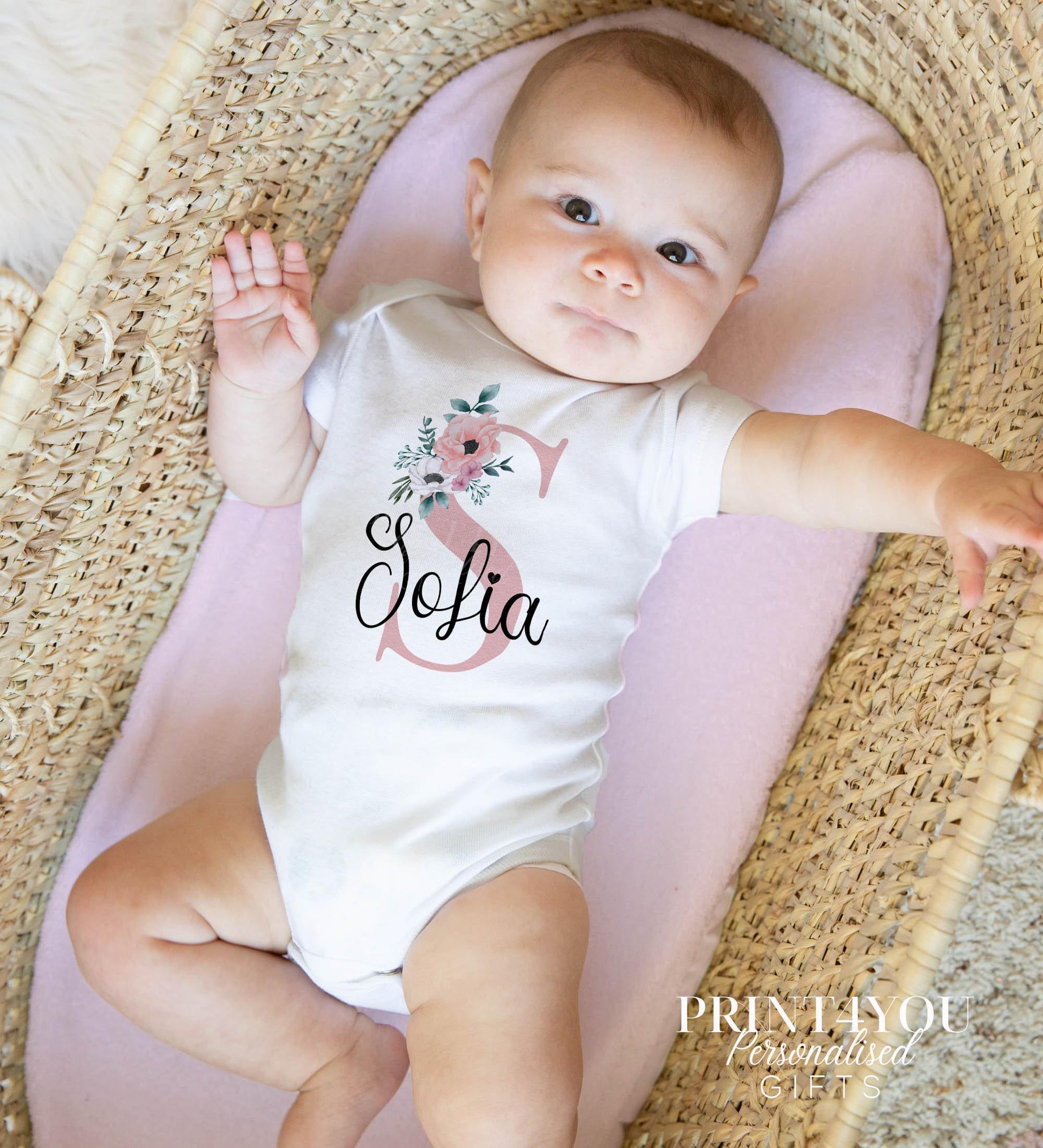 Personalised baby sleepsuit in white cotton, printed with a pink floral design and custom initial on the chest.