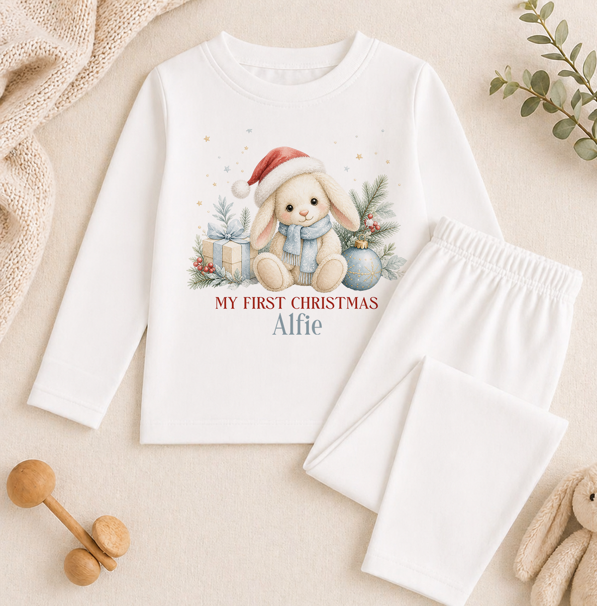 A white long-sleeved shirt with a Christmas-themed design, including a bunny wearing a Santa hat and surrounded by holiday decorations, is displayed on a beige background.