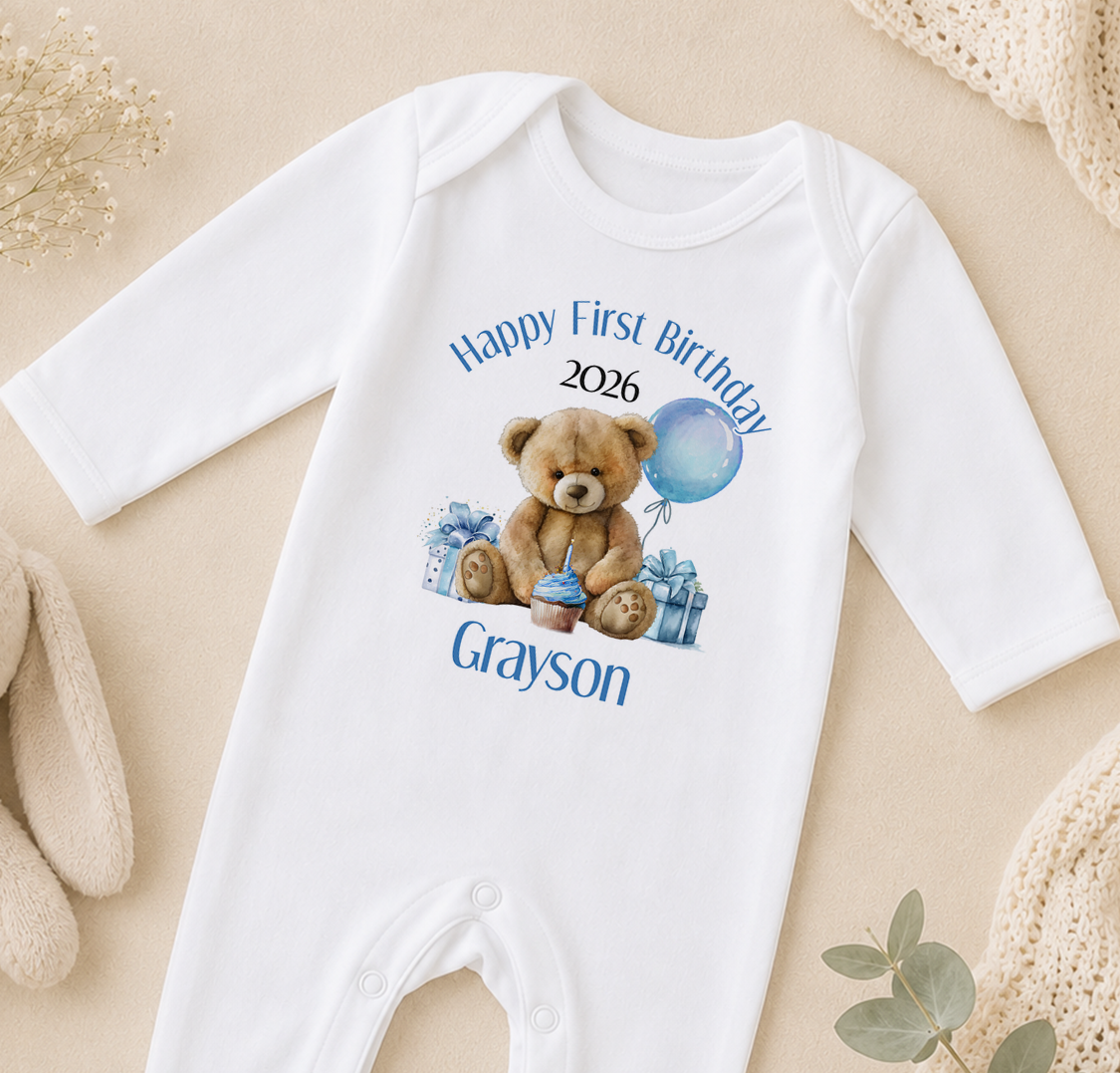 A white onesie with a teddy bear and a blue balloon, along with the text "Happy First Birthday Grayson" printed on it.