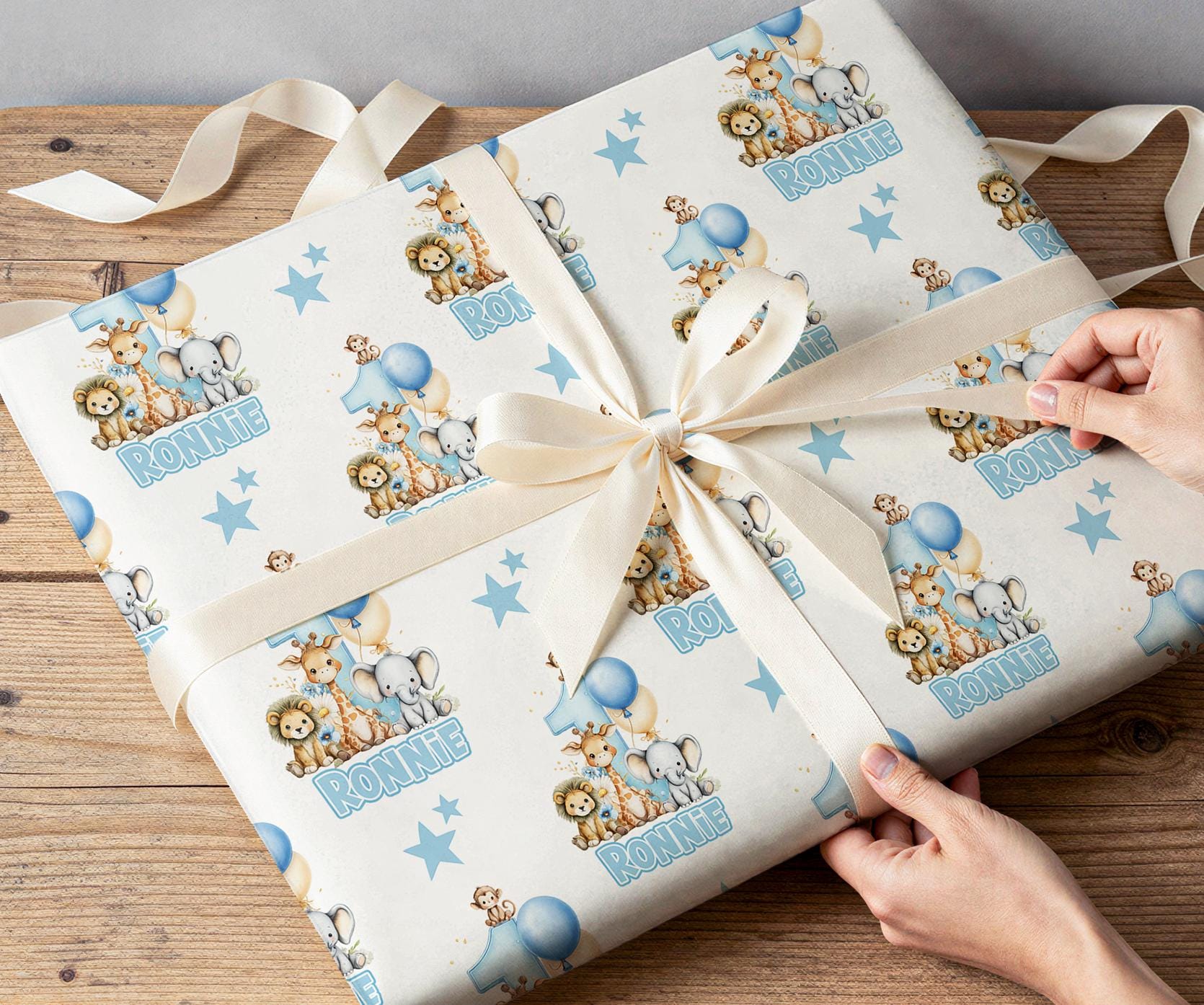 A person's hands are wrapping a gift with a white ribbon and a patterned wrapping paper featuring cartoon animal illustrations.