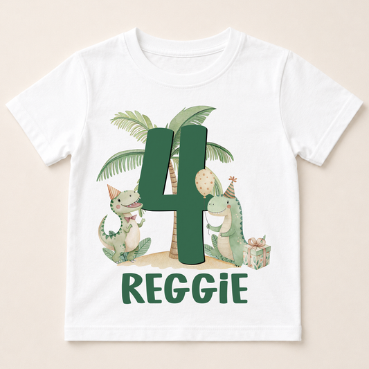 A white t-shirt with a graphic design featuring two dinosaurs, one larger than the other, and a palm tree. The larger dinosaur is wearing a party hat and holding a party balloon, while the smaller dinosaur is holding a gift box. The number "4" is prominently displayed in the center of the design. The text "REGGIE" is written below the image.