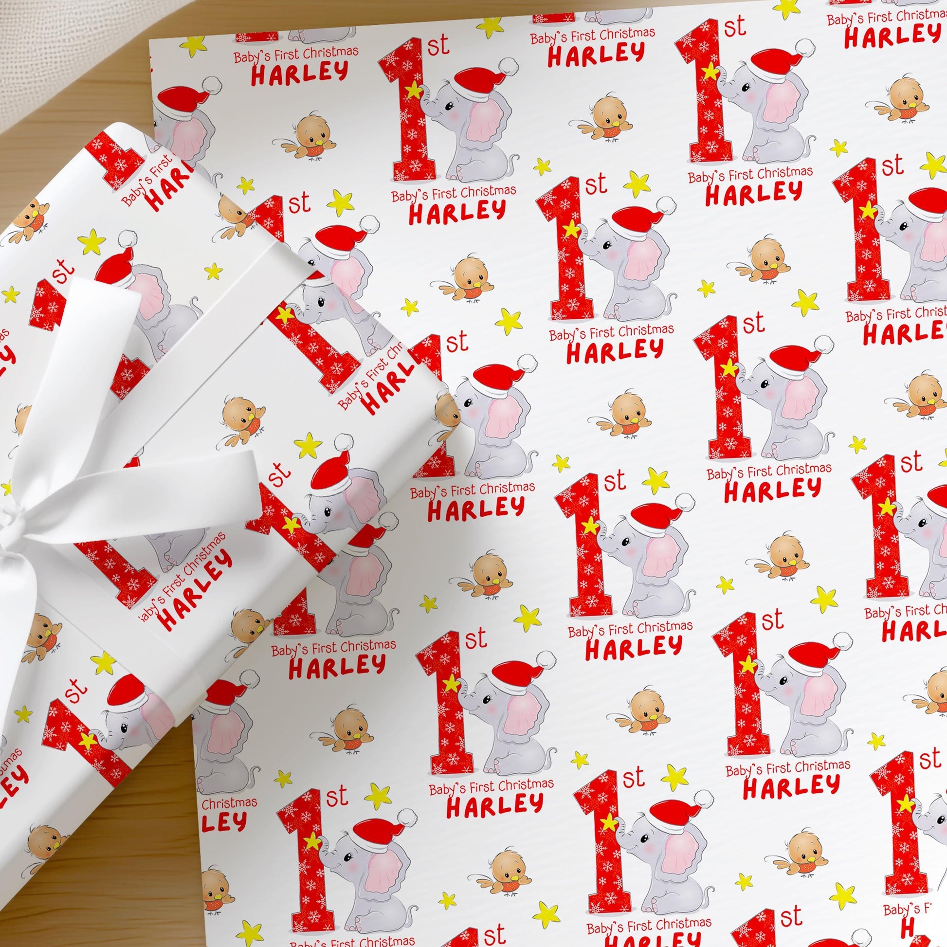 Personalised Baby's First Christmas wrapping paper featuring an elephant in a Santa hat with a custom name and festive stars.