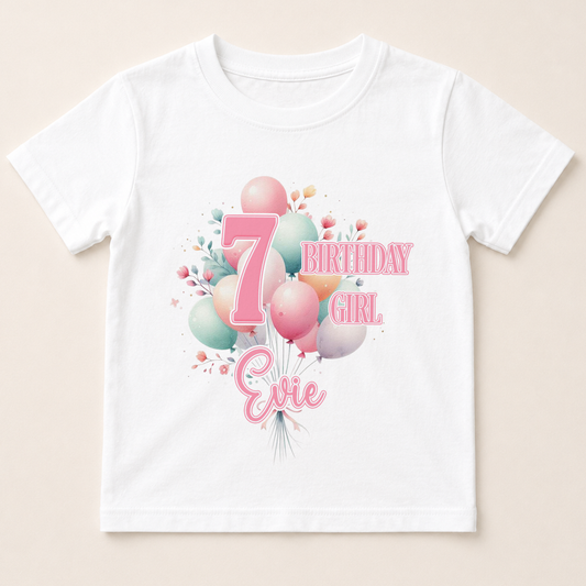 A white t-shirt with a graphic design featuring balloons and the number 7, along with the text "7 BIRTHDAY GIRL Evie" printed on it.