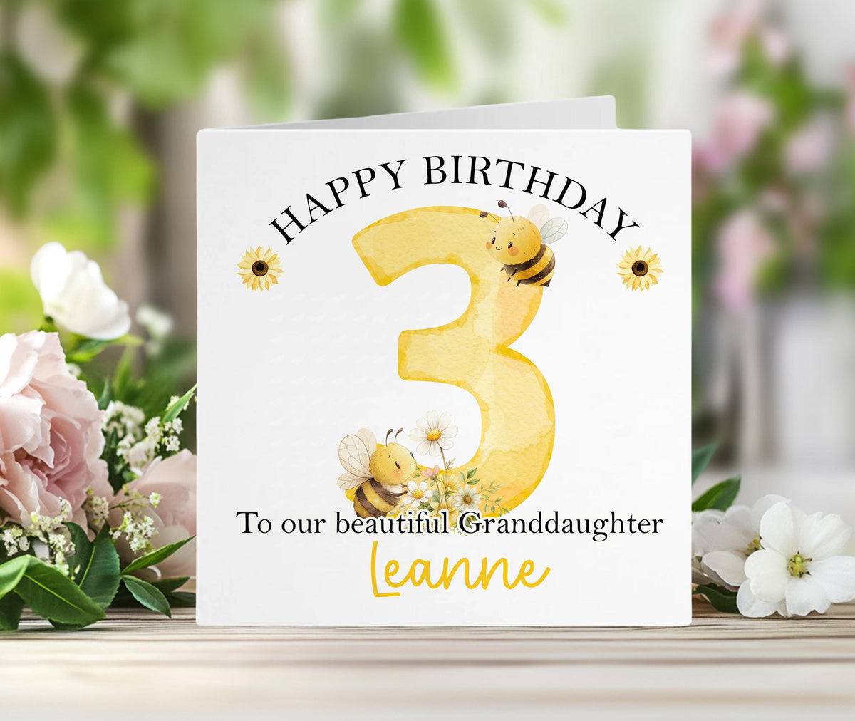 Personalised bumblebee birthday card with a large yellow number, bees and sunflowers, and custom name printed on the front, shown with its white envelope