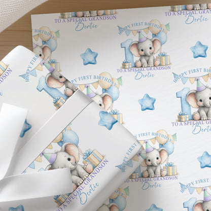 Close-up of personalised first birthday wrapping paper featuring a cute baby elephant, blue number one, balloons and presents on premium white wrapping paper.