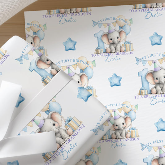 Close-up of personalised first birthday wrapping paper featuring a cute baby elephant, blue number one, balloons and presents on premium white wrapping paper.