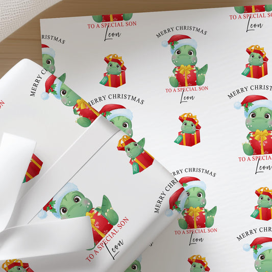 Close-up of personalised Christmas dinosaur wrapping paper featuring a cute T-Rex wearing a Santa hat with festive presents on premium white gift wrap.