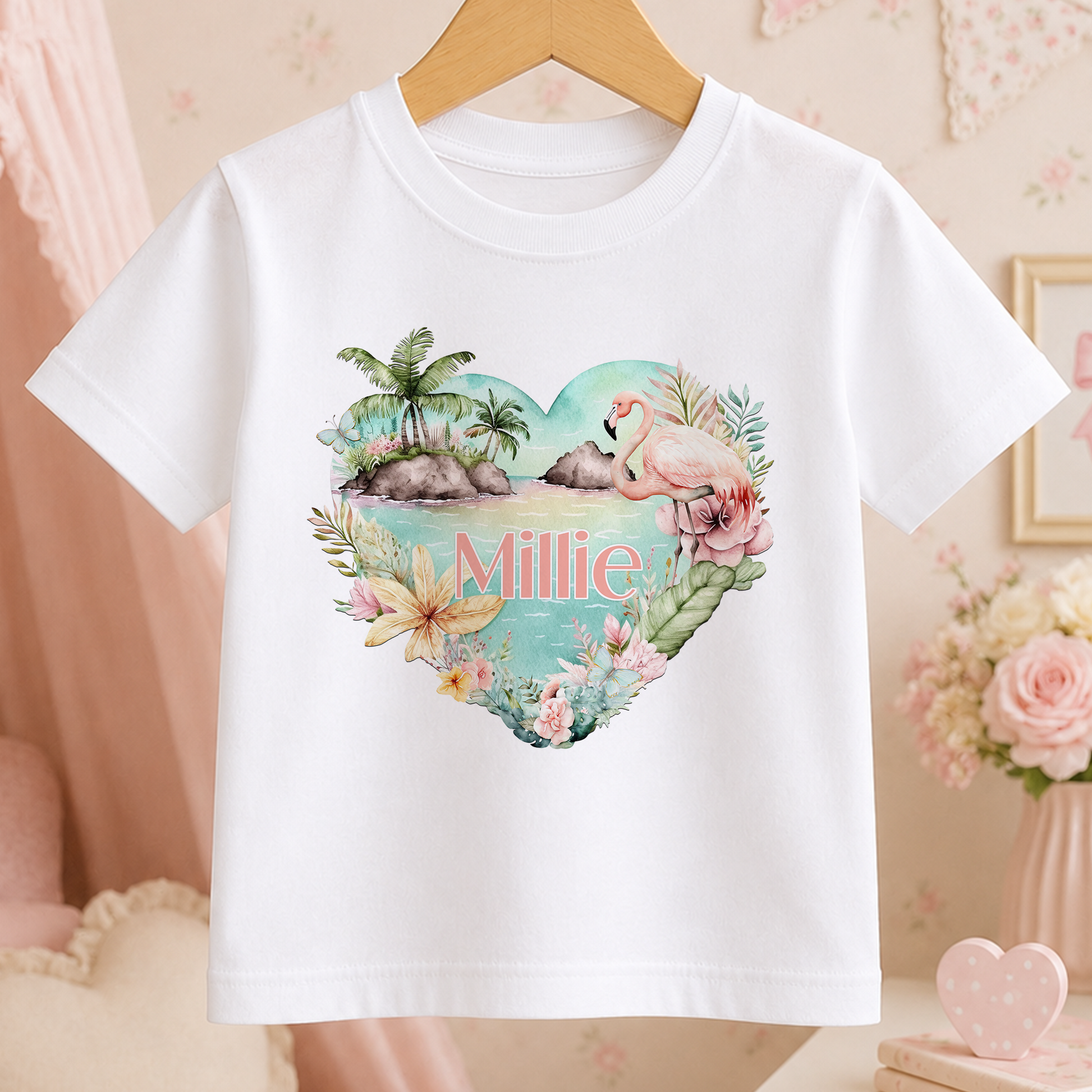 A white t-shirt with a heart-shaped design featuring a flamingo, palm trees, and flowers, along with the name "Millie" written on it.