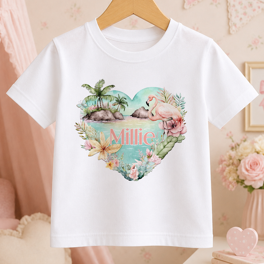 A white t-shirt with a heart-shaped design featuring a flamingo, palm trees, and flowers, along with the name "Millie" written on it.
