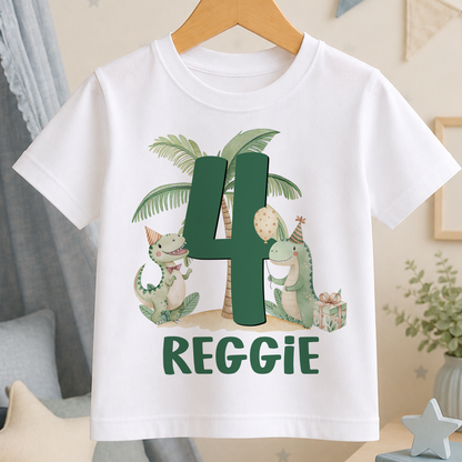 A white t-shirt with a green dinosaur graphic and the number "4" printed on it, along with the text "REGGIE".