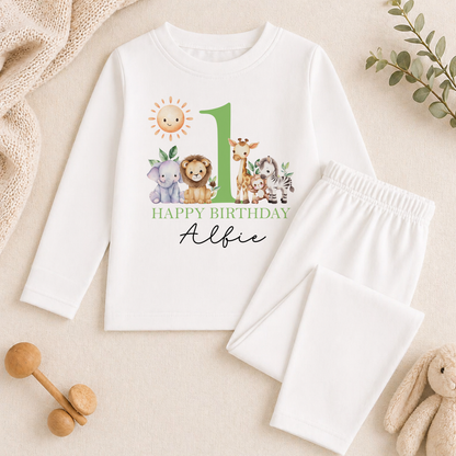 Long-sleeved top and white trousers from the safari friends birthday set, printed with jungle animals and 'Happy Birthday Albie', styled with baby toys and greenery.