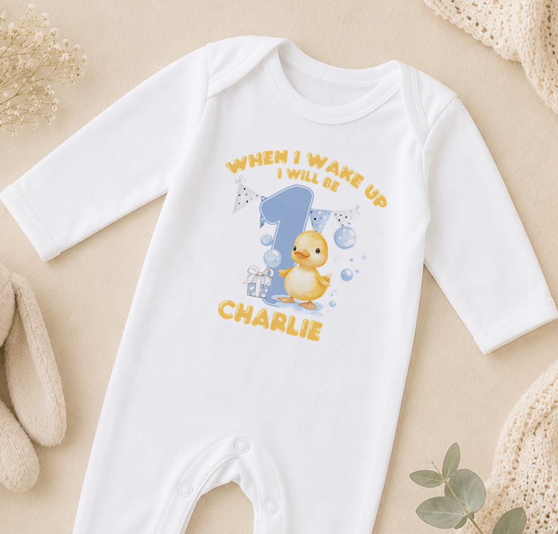 A white onesie with a yellow duck and the text "WHEN I WAKE UP I WILL BE CHARLIE" printed on it.