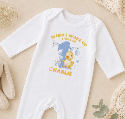 A white onesie with a yellow duck and the text "WHEN I WAKE UP I WILL BE CHARLIE" printed on it.