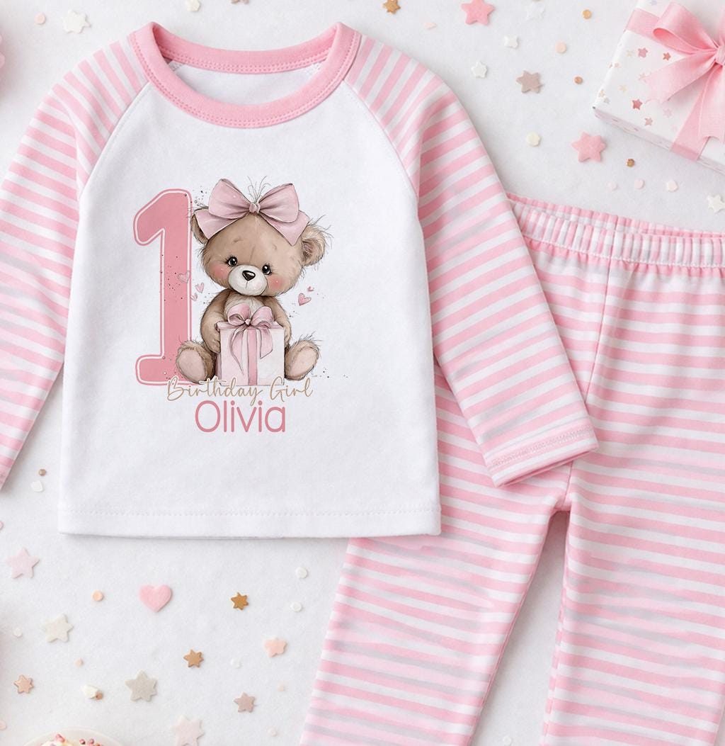 Personalised first birthday pyjamas with pink teddy bear design and custom name, soft white cotton.