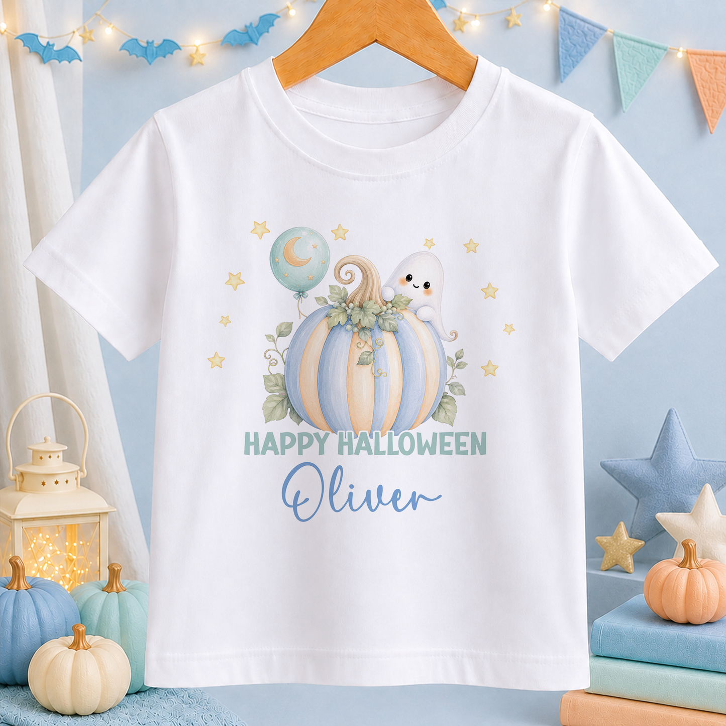 A white t-shirt with a Halloween-themed graphic design, including a pumpkin, ghost, and stars, along with the text "Happy Halloween Oliver". The t-shirt is hanging on a wooden hanger, and there are other Halloween decorations and items in the background.