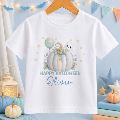 A white t-shirt with a Halloween-themed graphic design, including a pumpkin, ghost, and stars, along with the text "Happy Halloween Oliver". The t-shirt is hanging on a wooden hanger, and there are other Halloween decorations and items in the background.