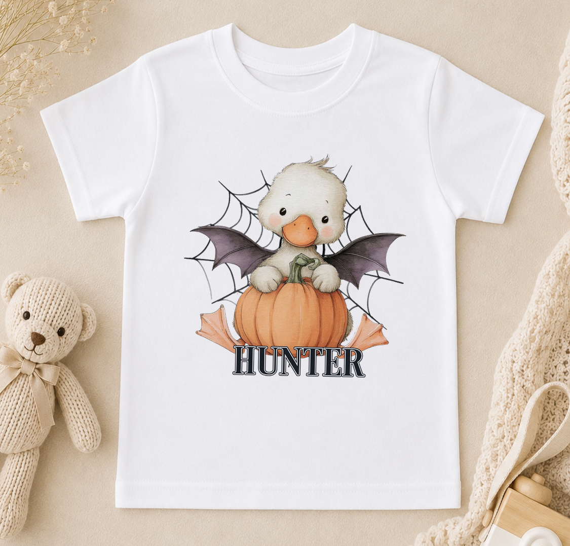 A white t-shirt with a cartoon image of a duck holding a pumpkin and a spider web, with the word "Hunter" written below.