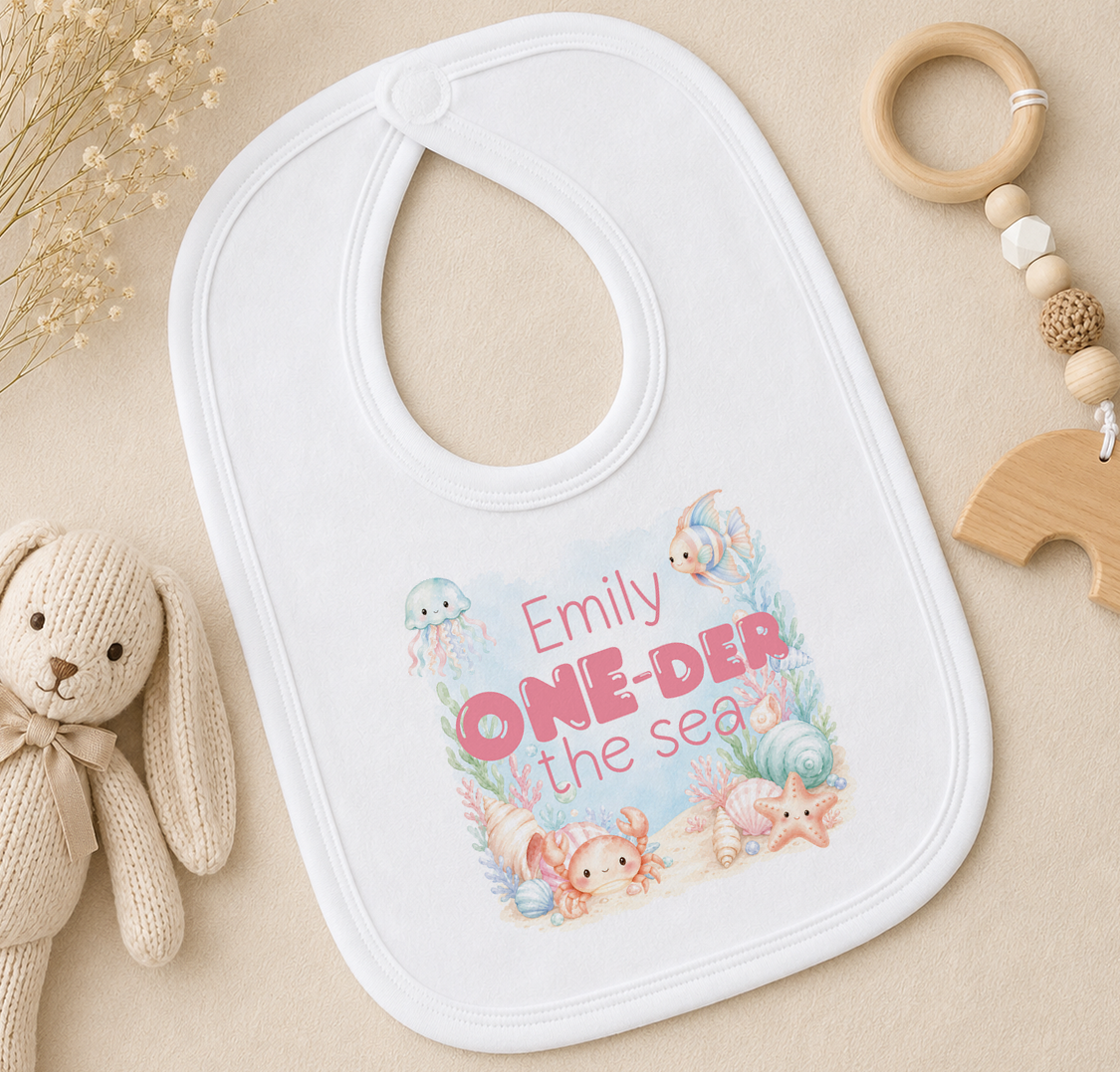 Personalised baby bib with an underwater scene and the child's printed name, styled with a soft toy