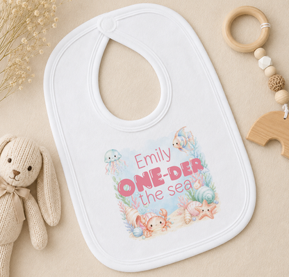 Personalised baby bib with an underwater scene and the child's printed name, styled with a soft toy