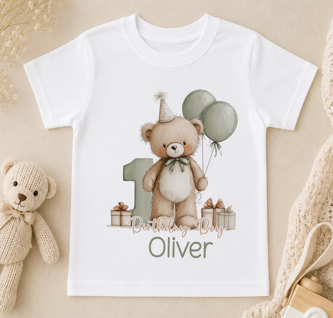 A white t-shirt with a teddy bear wearing a party hat and holding balloons, along with the text "Birthday Boy Oliver" printed on it.