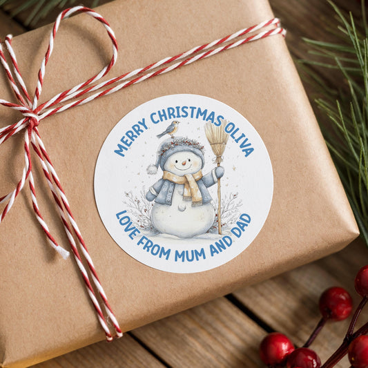 A brown gift box with a white label featuring a snowman and the text "Merry Christmas Oliva" and "Love from MUM and Dad".