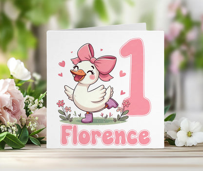 Personalised 1st birthday card for a baby girl with a pink duck wearing a bow and boots, and the child's custom name printed on the front