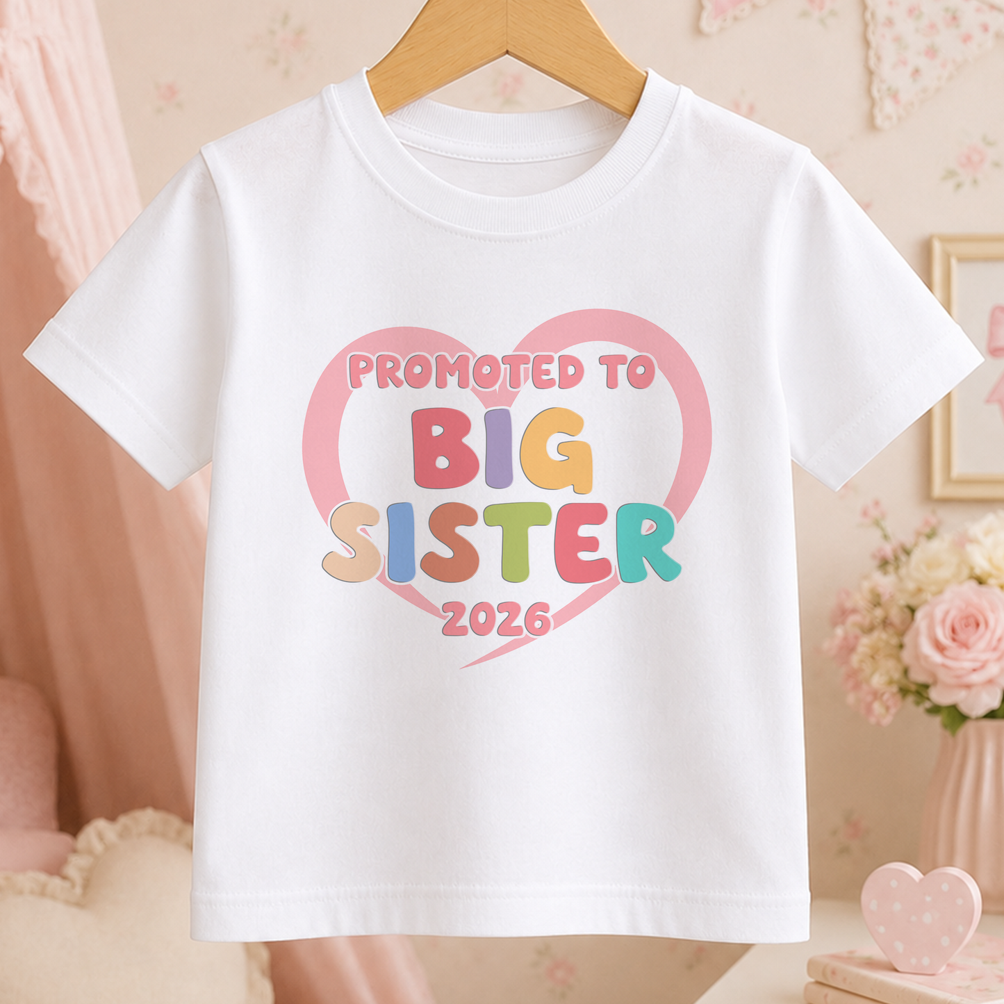 A white t-shirt with a heart-shaped graphic and text that says "Promoted to Big Sister 2026".
