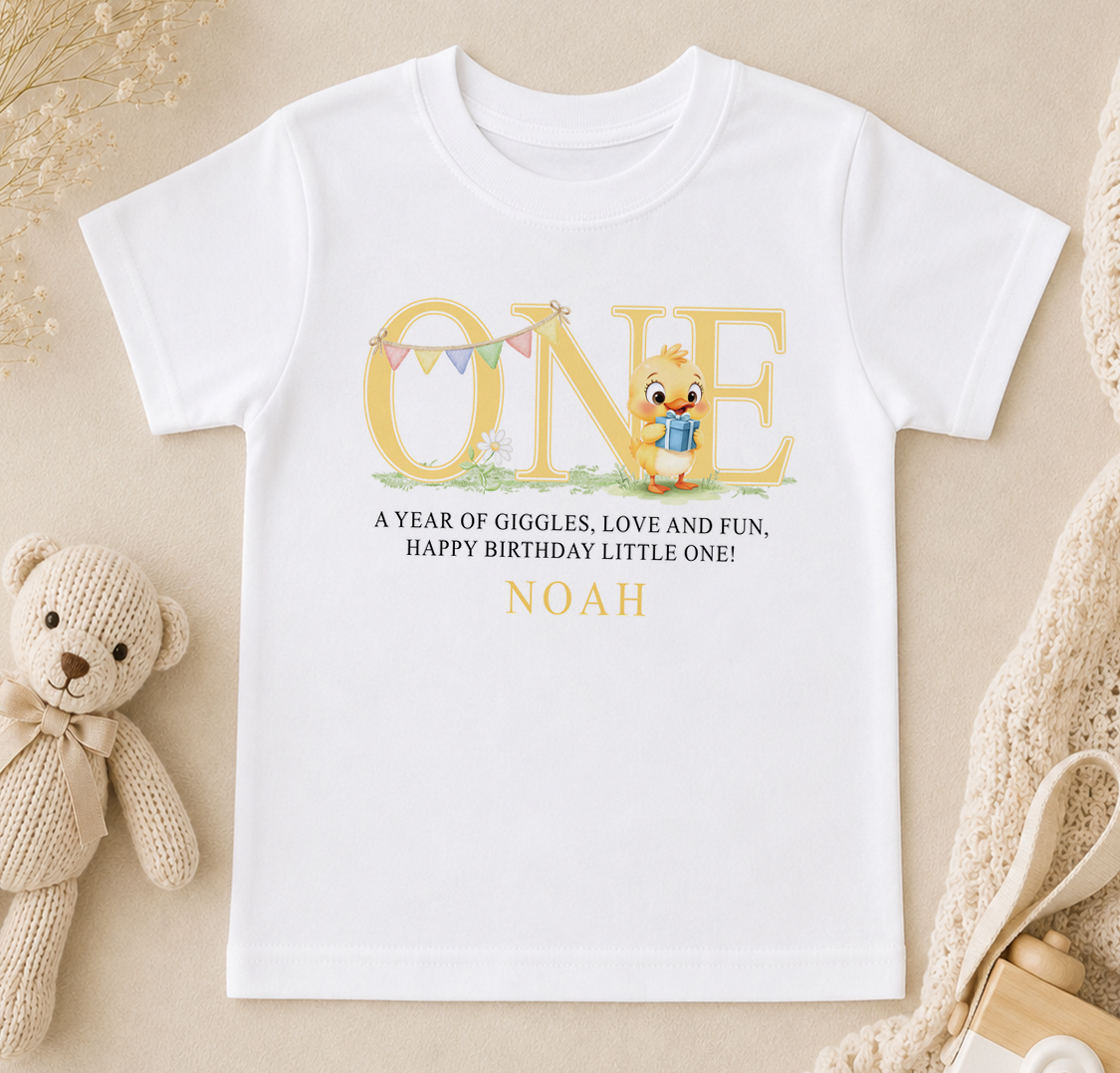 A white t-shirt with a personalized message and a cartoon duck graphic, along with a teddy bear and other baby-related items.