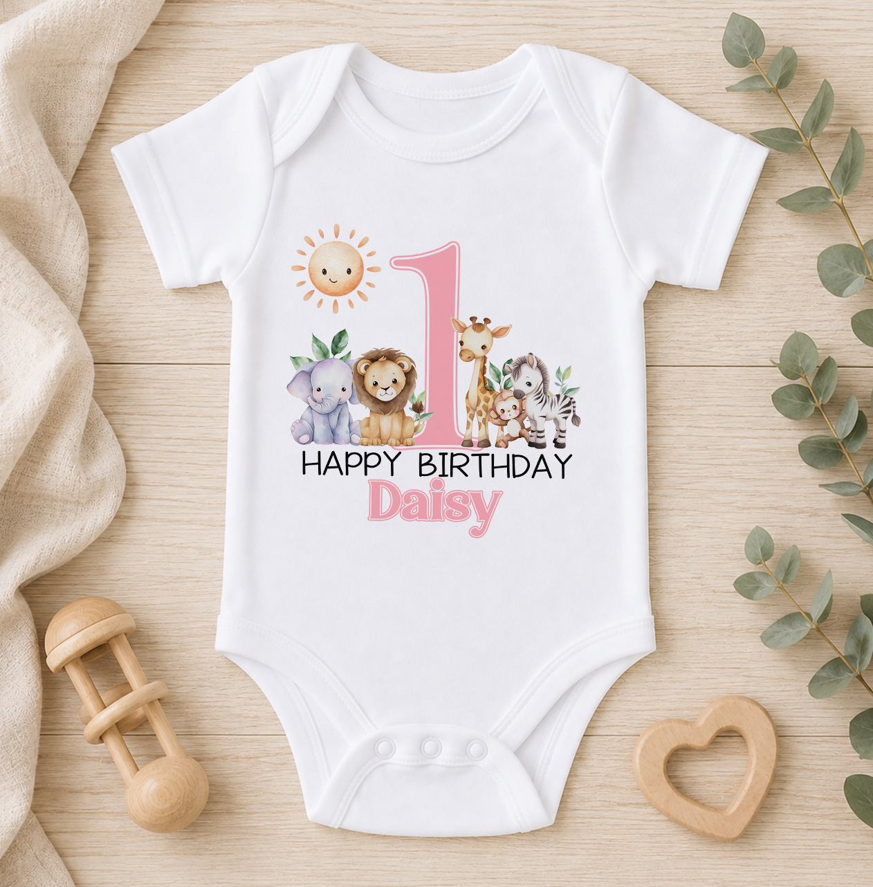 A white onesie with a pink number 1 and a design of various animals, including a lion, giraffe, and elephant, along with the text "Happy Birthday Daisy".