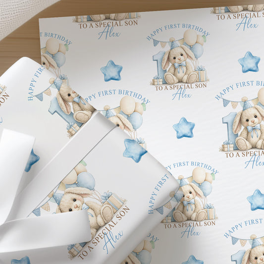 Close-up of personalised first birthday wrapping paper featuring a cute bunny rabbit, blue number one, balloons and presents on premium white wrapping paper.