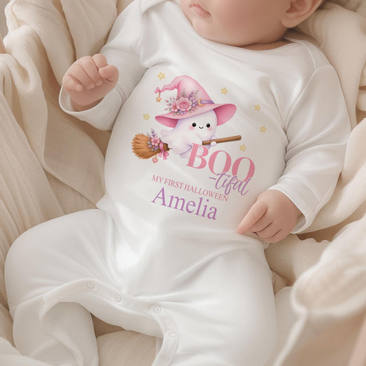 Personalised baby’s first Halloween white sleepsuit featuring a cute flying ghost on a broomstick, pink witch hat, flowers, stars and baby’s name.