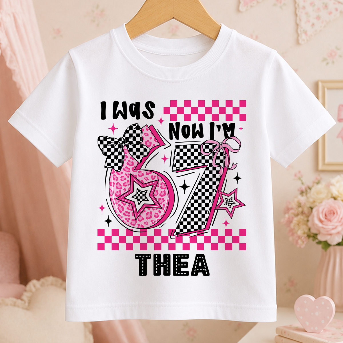 Pastel pink t-shirt with 'I Was 6, Now I'm 7' birthday design, personalised with the name Thea, surrounded by stars and checkerboard pattern