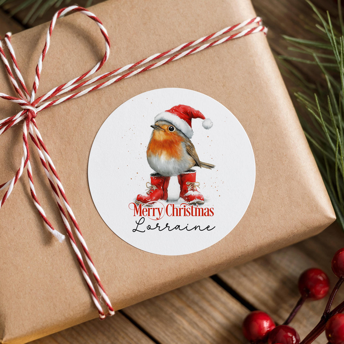 Personalised robin Christmas sticker in a Santa hat and red boots, stuck on a rustic gift box wrapped with twine and pine branches