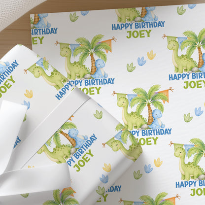 Personalised dinosaur wrapping paper sheet laid flat showing the full repeating dinosaur and tropical tree pattern with name.