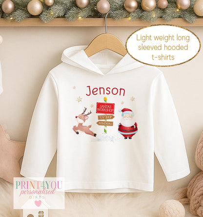 Personalised Christmas hooded t-shirt for kids, white lightweight long sleeved hoodie printed with Santa beside a North Pole signpost and a name
