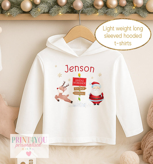 Personalised Christmas hooded t-shirt for kids, white lightweight long sleeved hoodie printed with Santa beside a North Pole signpost and a name