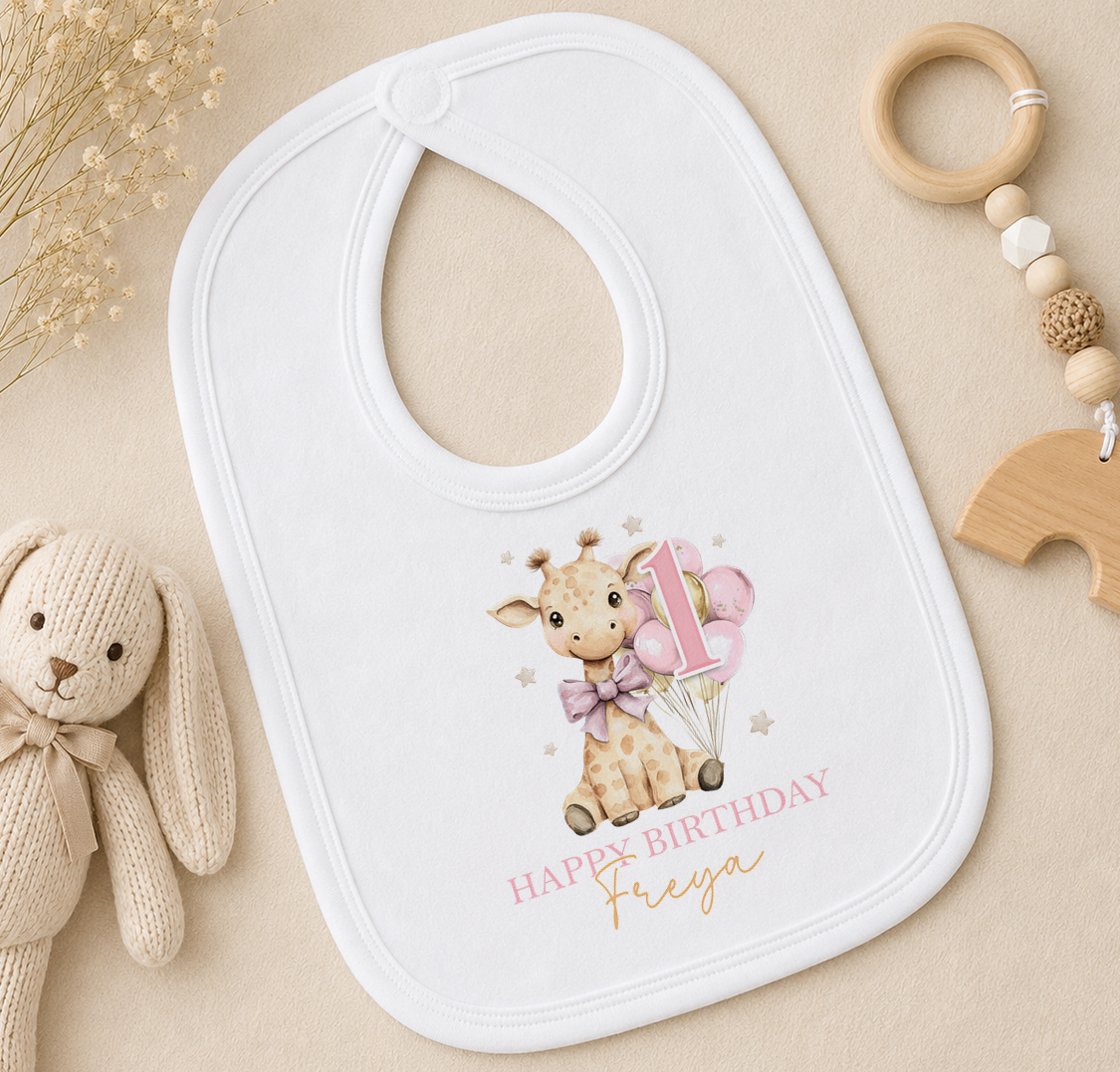 Personalised white bib printed with a giraffe and balloons, styled with a wooden toy and a wooden bead ring.