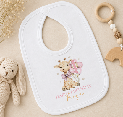 Personalised white bib printed with a giraffe and balloons, styled with a wooden toy and a wooden bead ring.