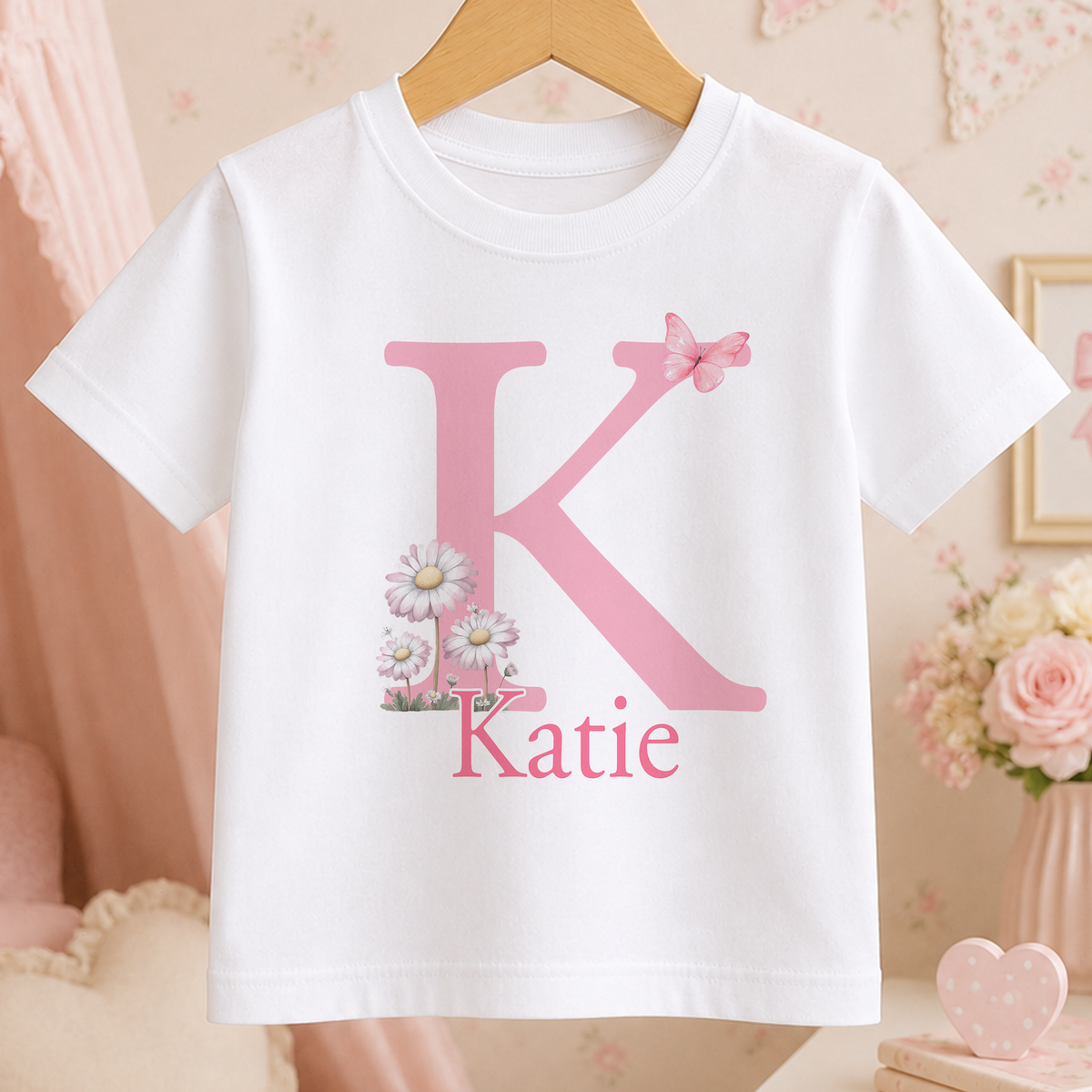 A white t-shirt with a pink letter "K" and a pink flower design, along with the name "Katie" printed below it.
