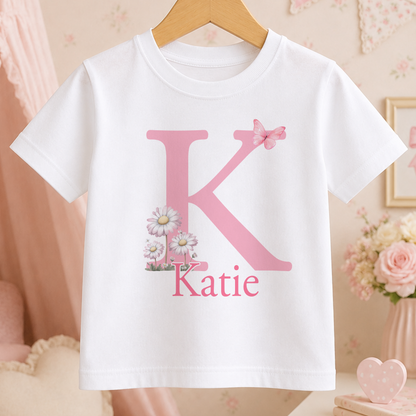 A white t-shirt with a pink letter "K" and a pink flower design, along with the name "Katie" printed below it.