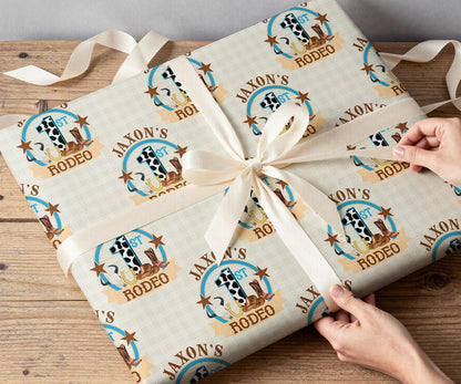 Hands wrapping a first birthday gift in personalised cowboy rodeo wrapping paper printed with 'Rodeo' and '1st'.