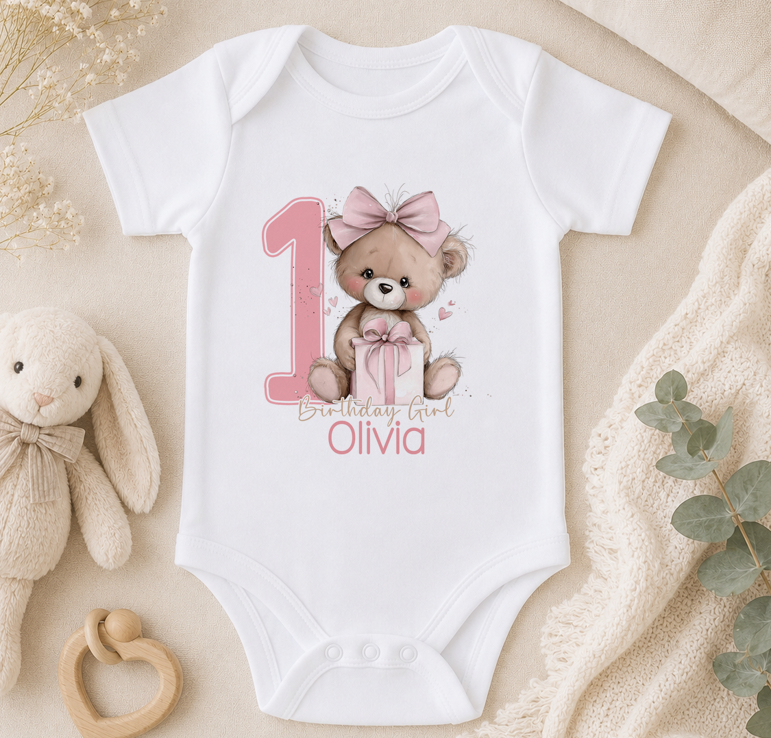 Personalised pink teddy bear first birthday vest styled with soft toys and a blanket.