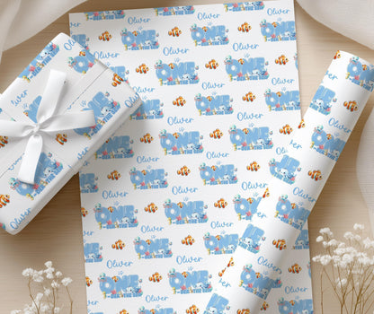 Personalised ocean wrapping paper with custom name and fish illustrations, displayed on a wooden surface with flowers