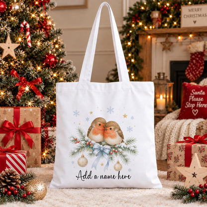 Personalised Christmas tote bag in white cotton with two robins on a pine branch, gold baubles and blue snowflakes, with a name beneath