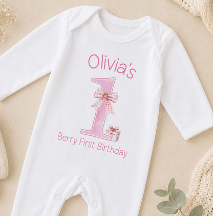 A white onesie with a pink number one and a bow, along with the text "Olivia's Berry First Birthday".